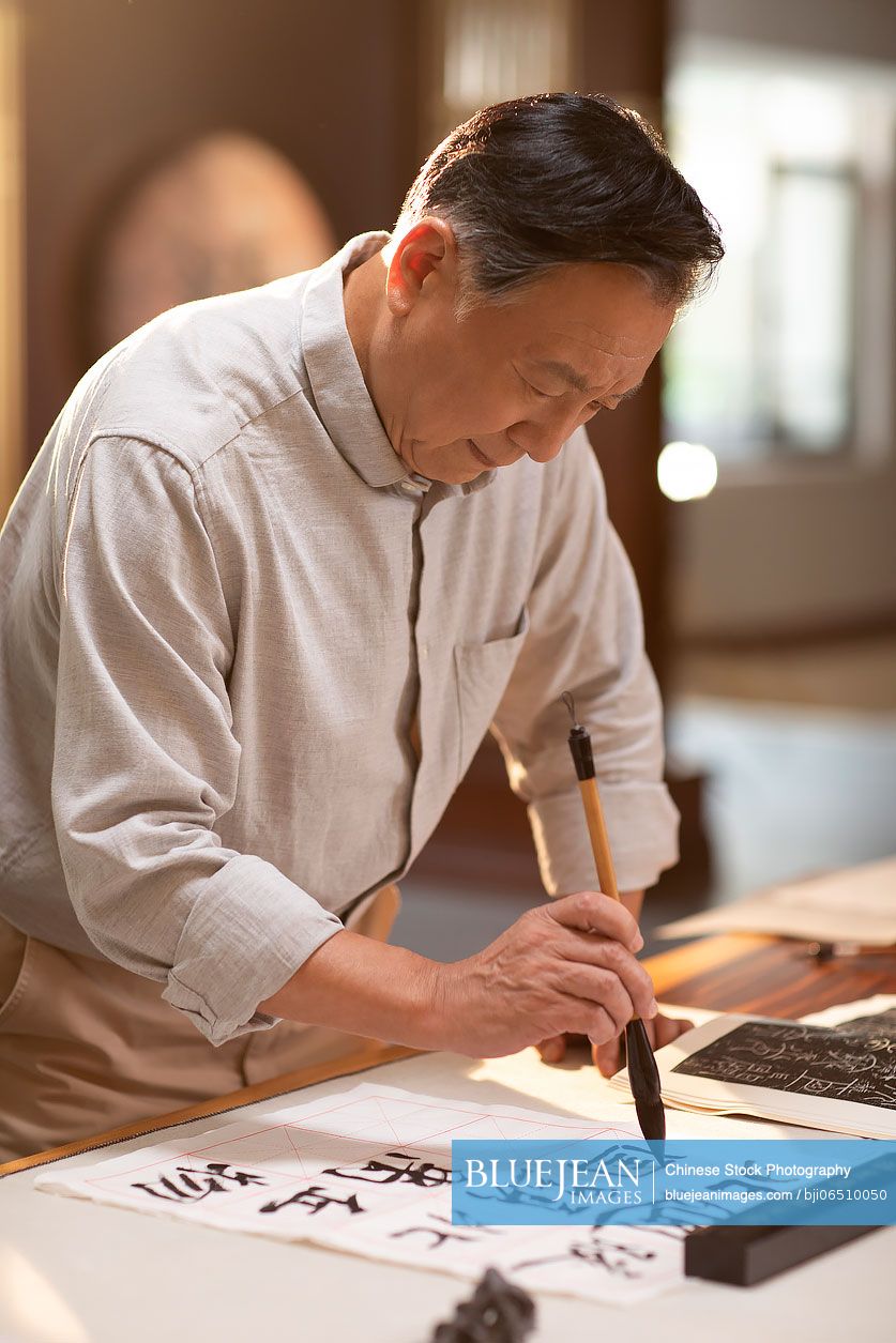 Senior Chinese man practicing calligraphy in the study