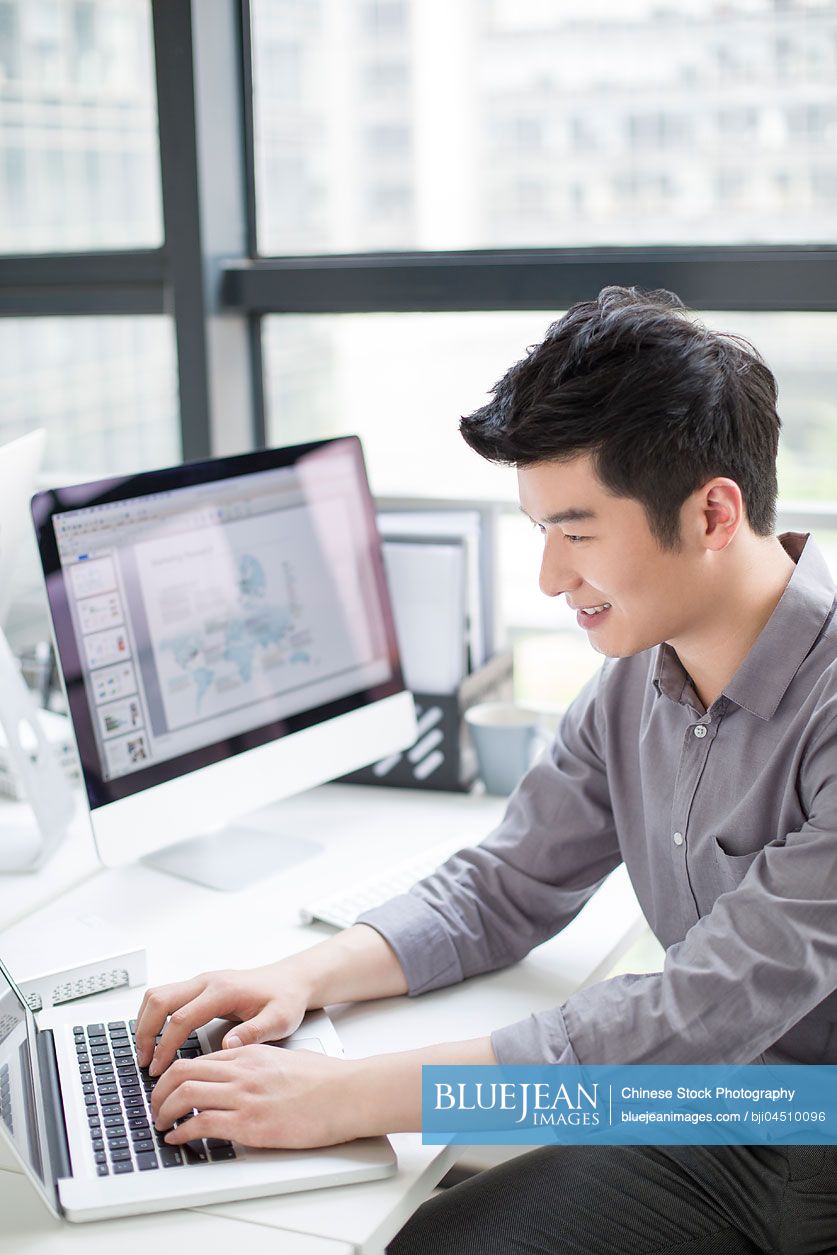 Young Chinese businessman using laptop in office