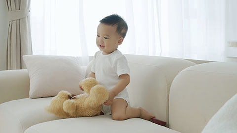 Baby playing with a toy bear on the sofa