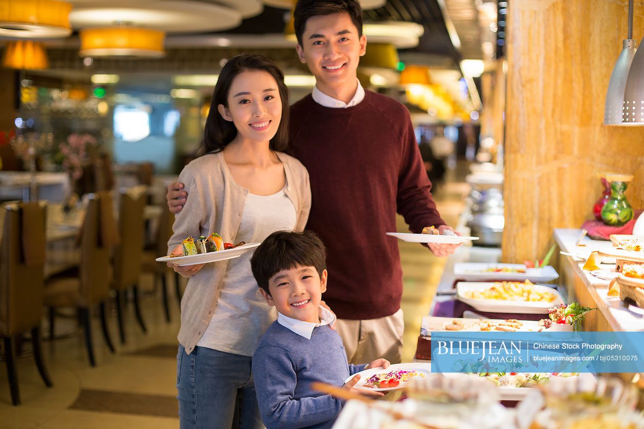 Cheerful young Chinese family taking food from buffet table