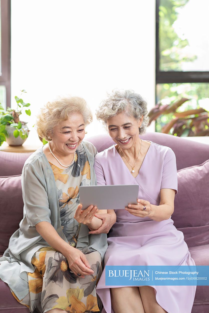 Happy senior Chinese friends using digital tablet at home