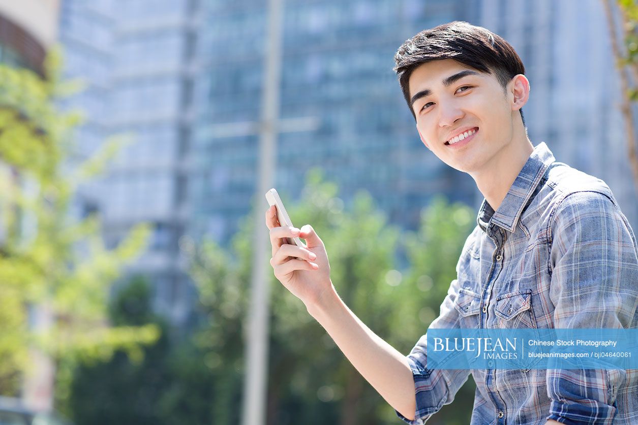 Happy young Chinese man holding a smart phone