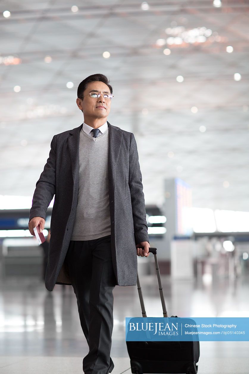 Chinese businessman pulling wheeled luggage in airport lobby
