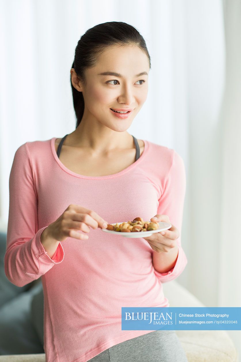 Happy young Chinese woman eating nuts
