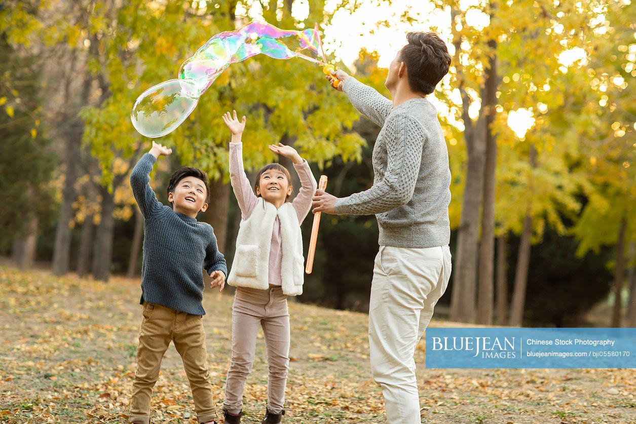 Happy young Chinese family playing with bubbles in autumn woods