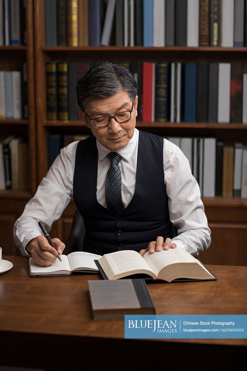 Senior Chinese businessman reading book in study