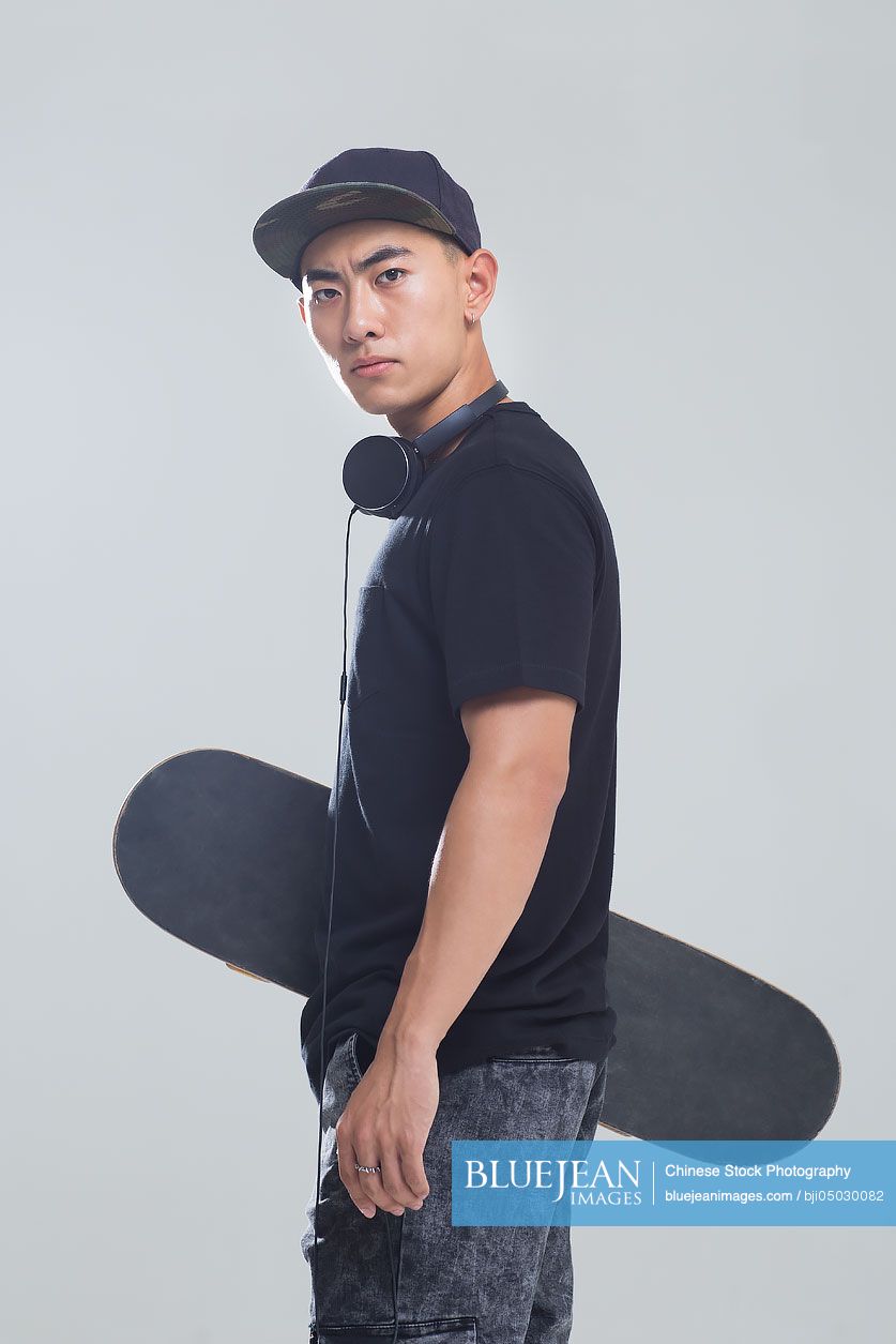 Portrait of young Chinese man with headphones holding a skateboard