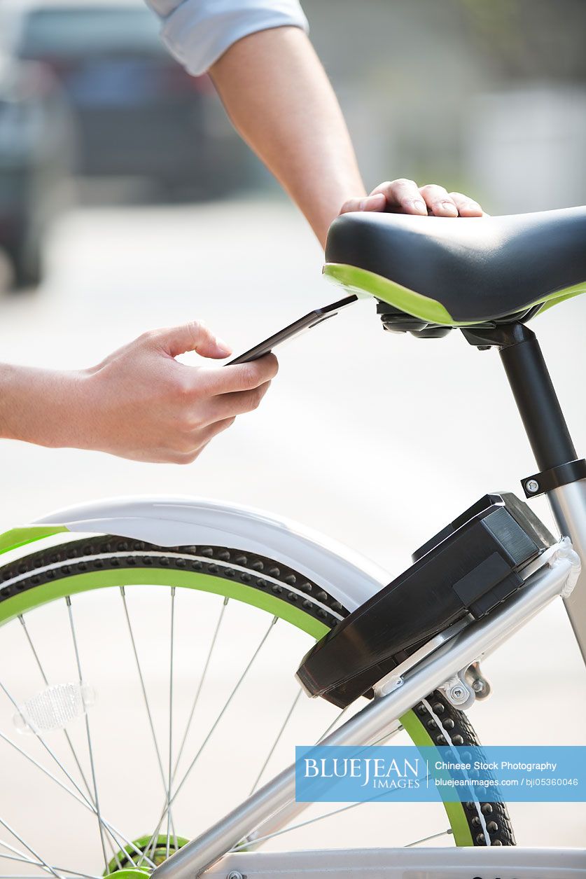 Young Chinese man scanning a QR code to unlock a share bike