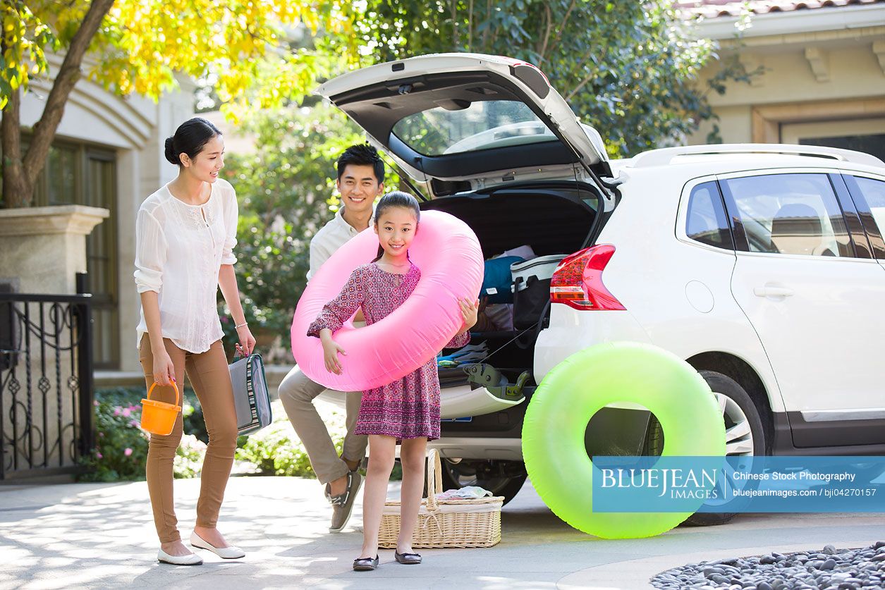 Young Chinese family putting water sports equipment into the car