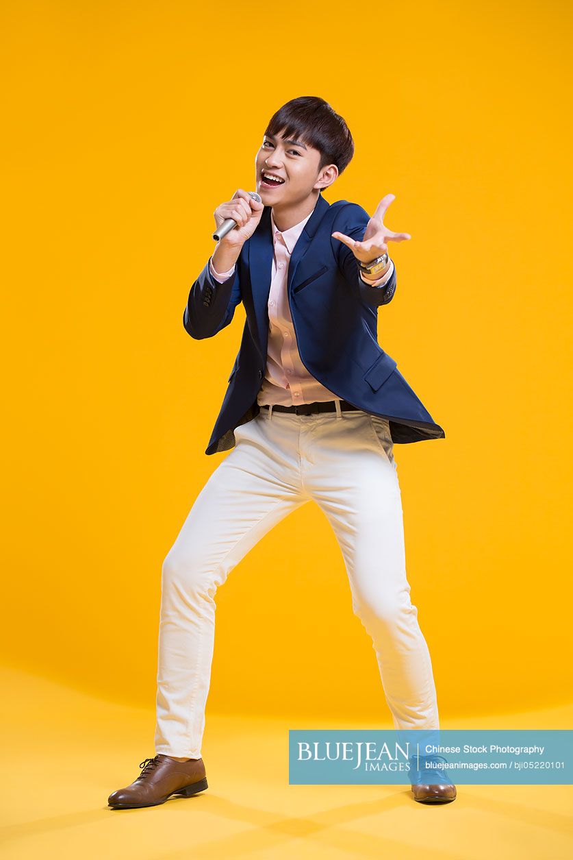 Cheerful young Chinese man singing with microphone