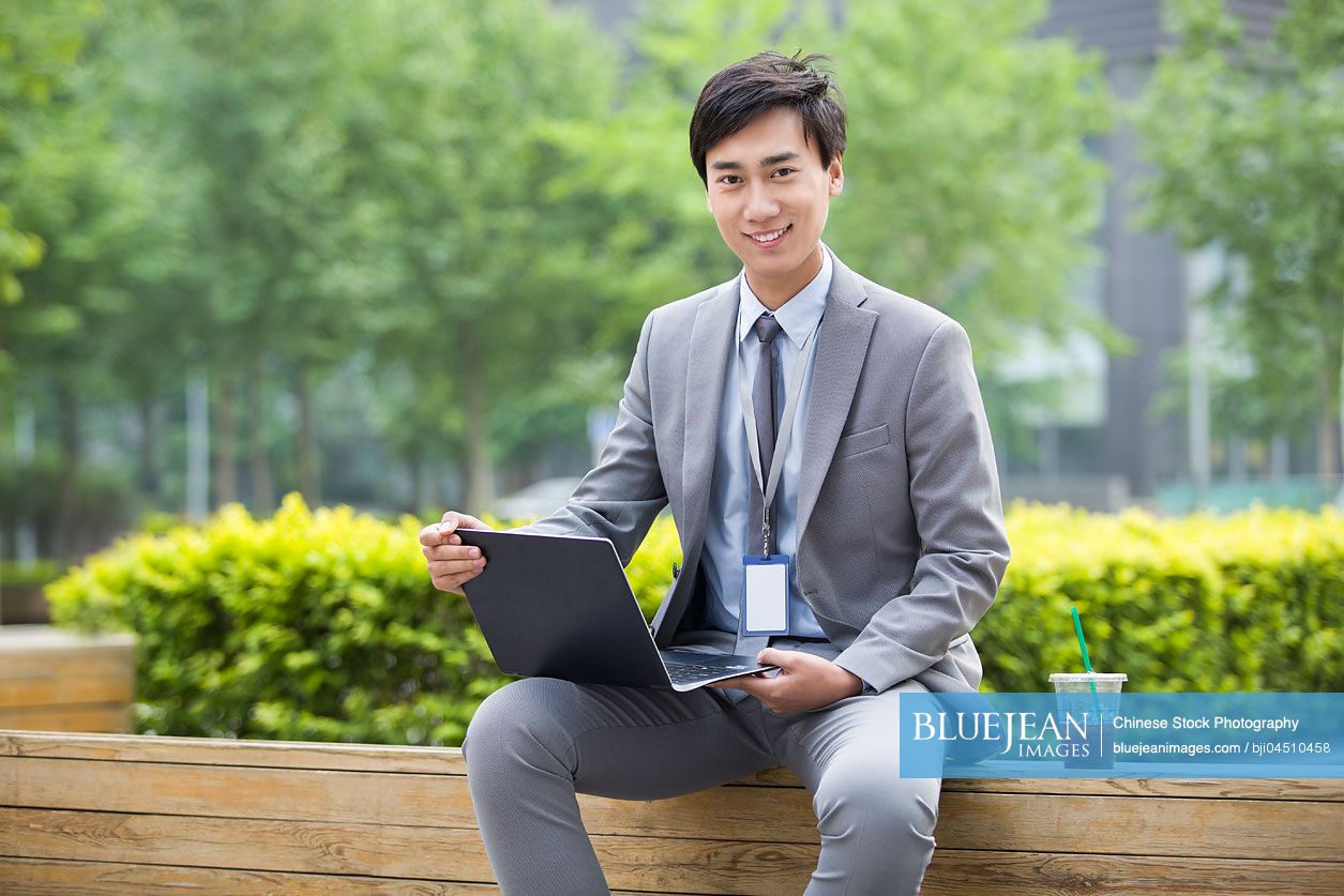 Young Chinese businessman working with laptop outdoors