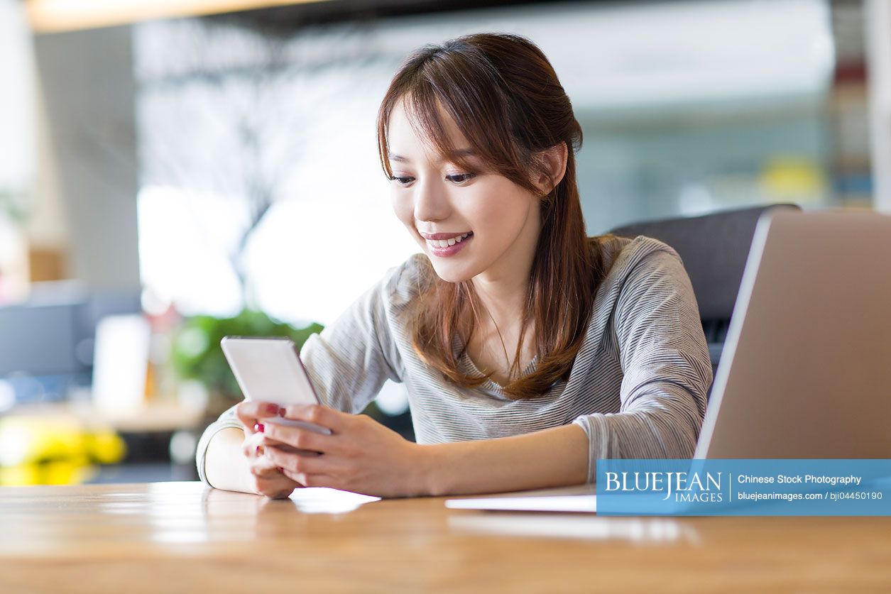 Young Chinese woman using smart phone in office