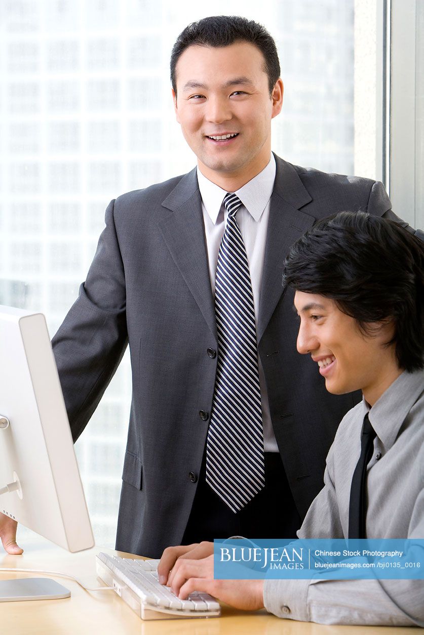 Chinese man in business suit shows young employee something on a computer