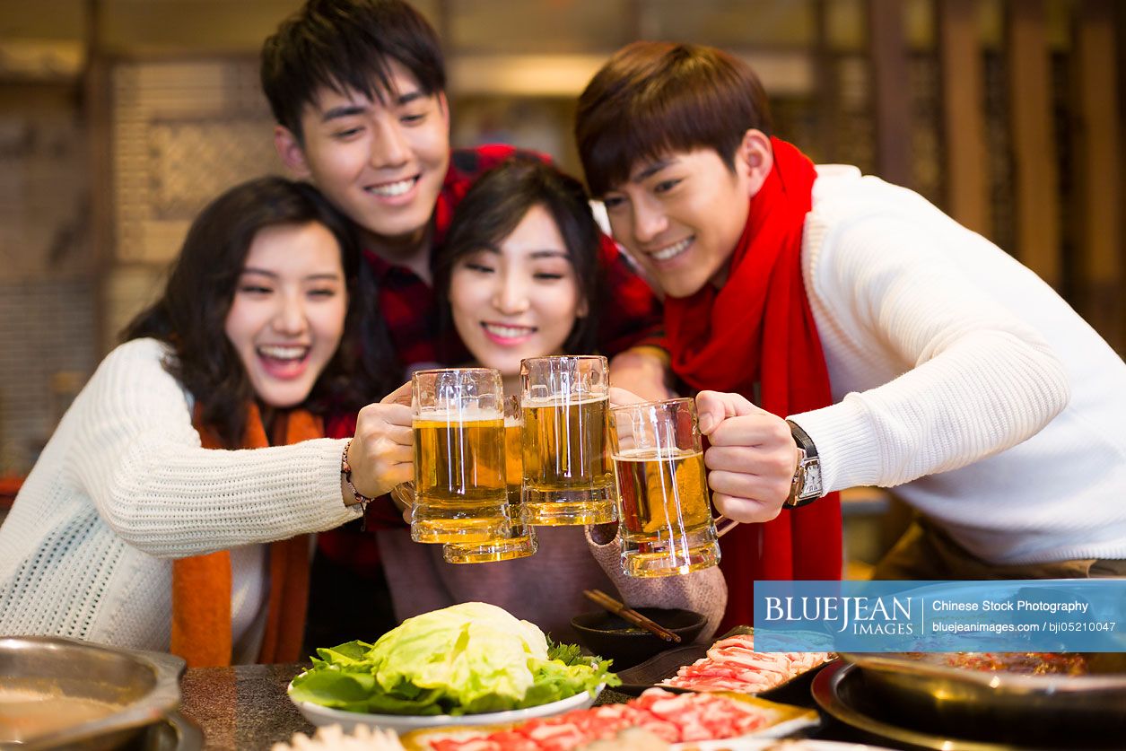 Young Chinese friends drinking beer in hotpot restaurant