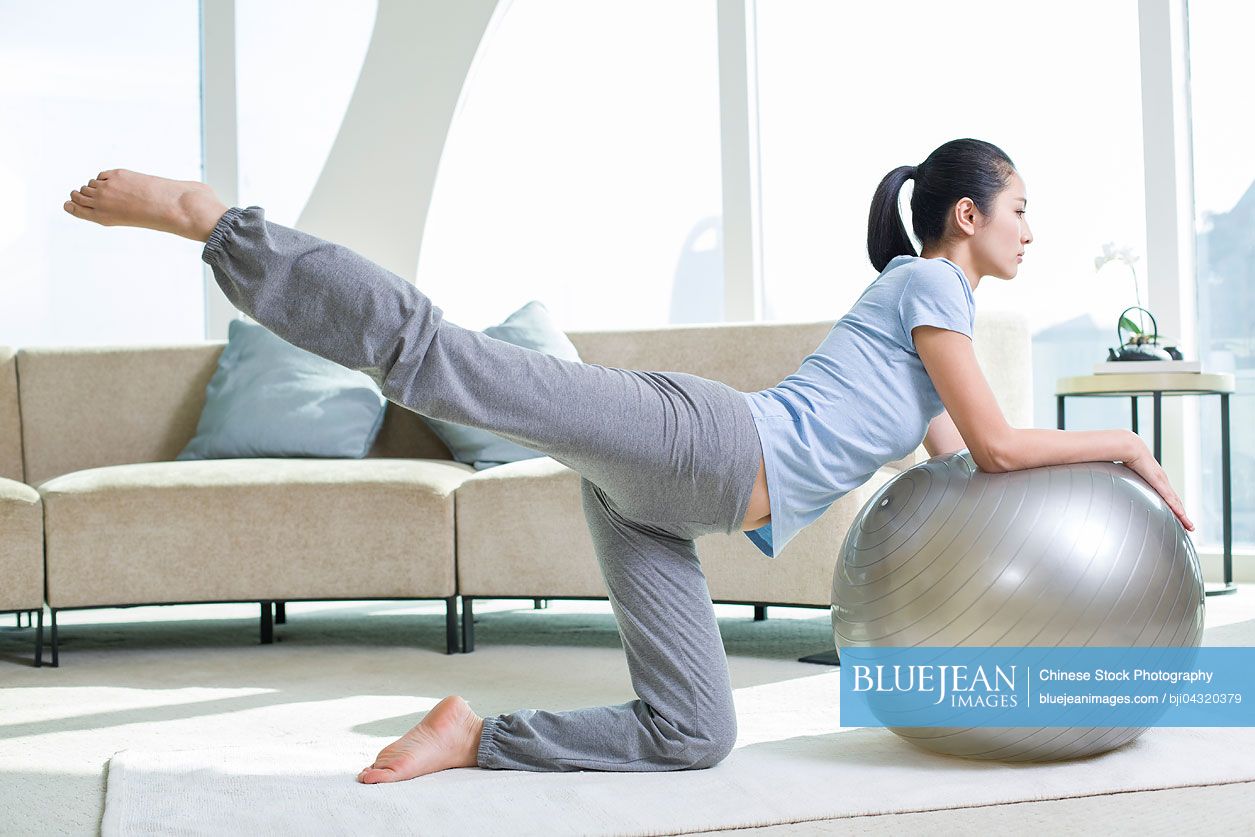 Young Chinese woman practicing yoga with fitness ball