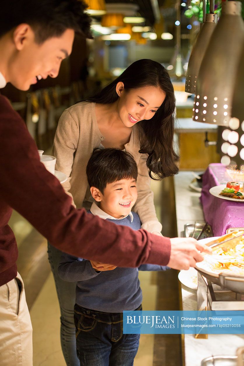 Cheerful young Chinese family taking food from buffet table