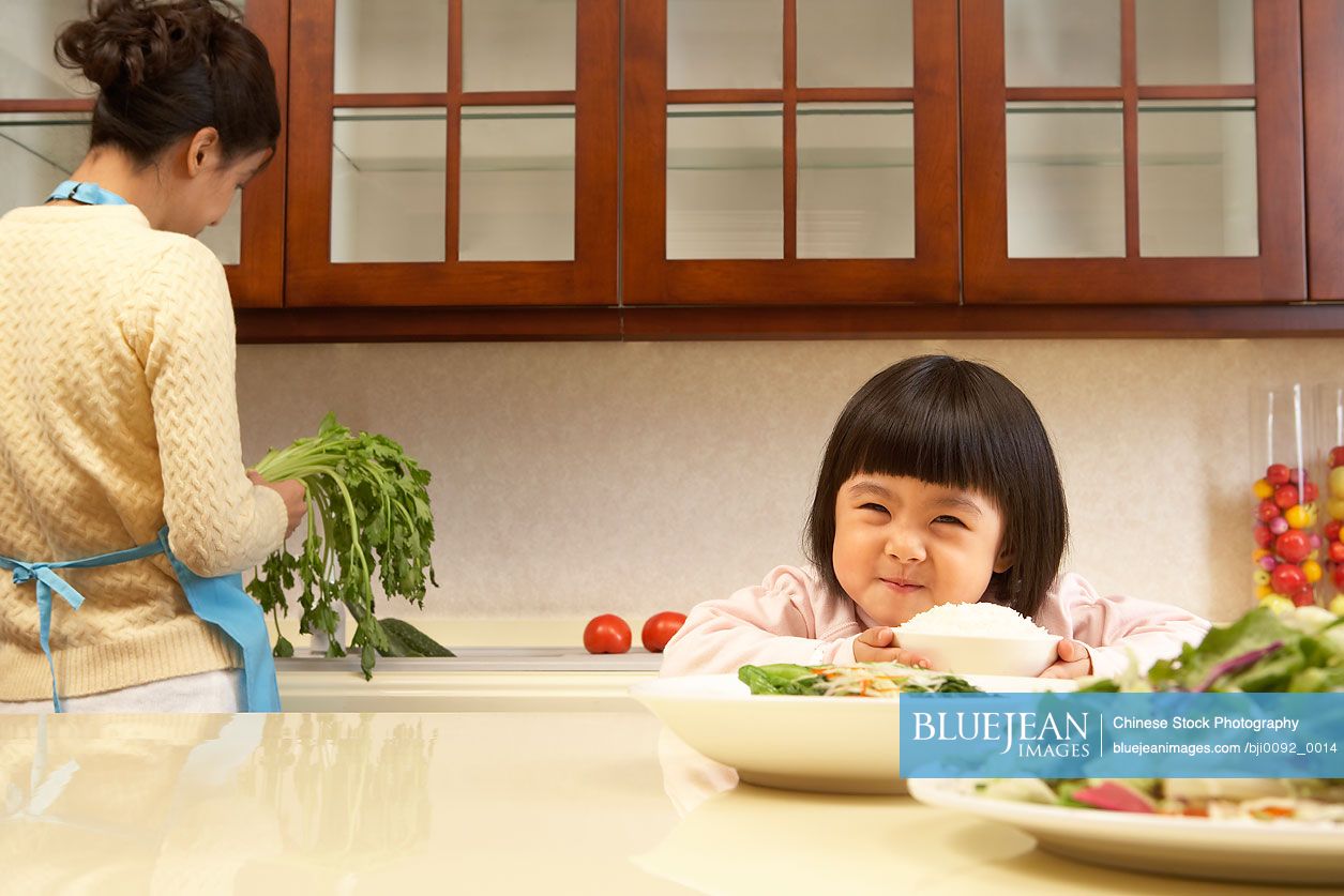 Young Chinese girl eating vegetables while her mother cooks