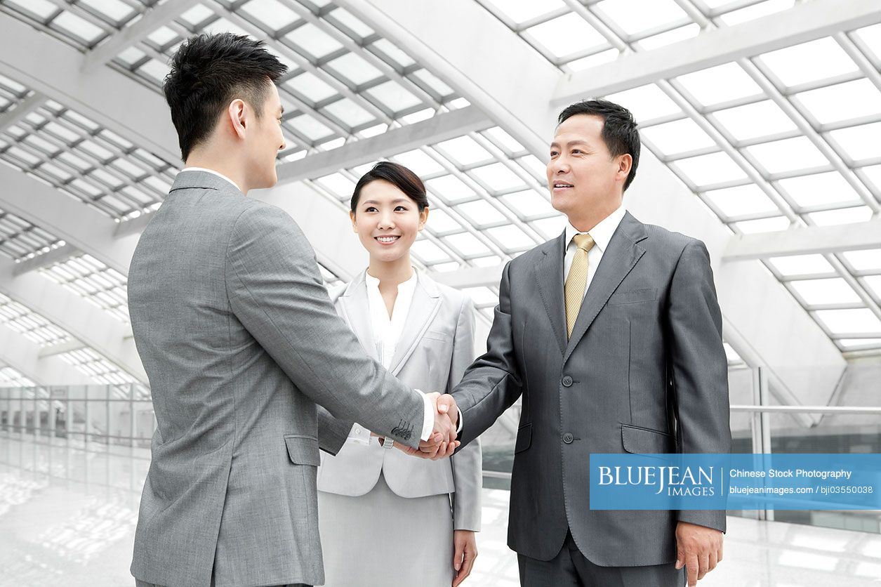 Chinese business people shaking hands in airport lobby