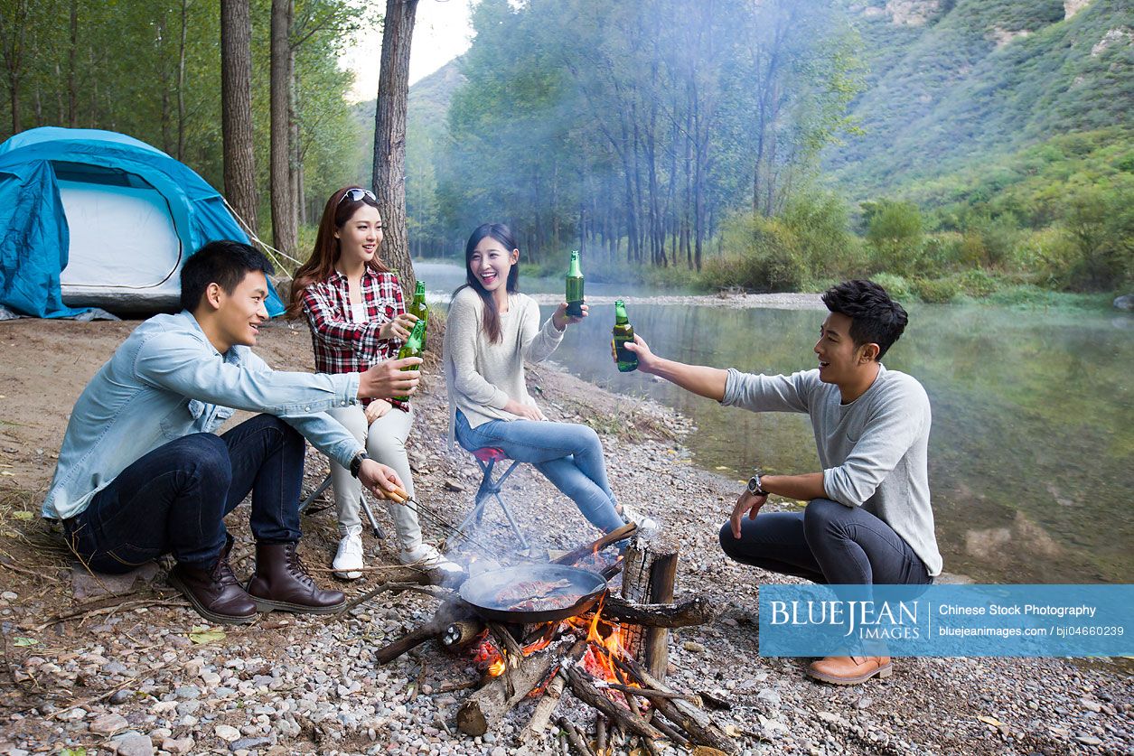 Young Chinese friends sitting around campfire drinking beer