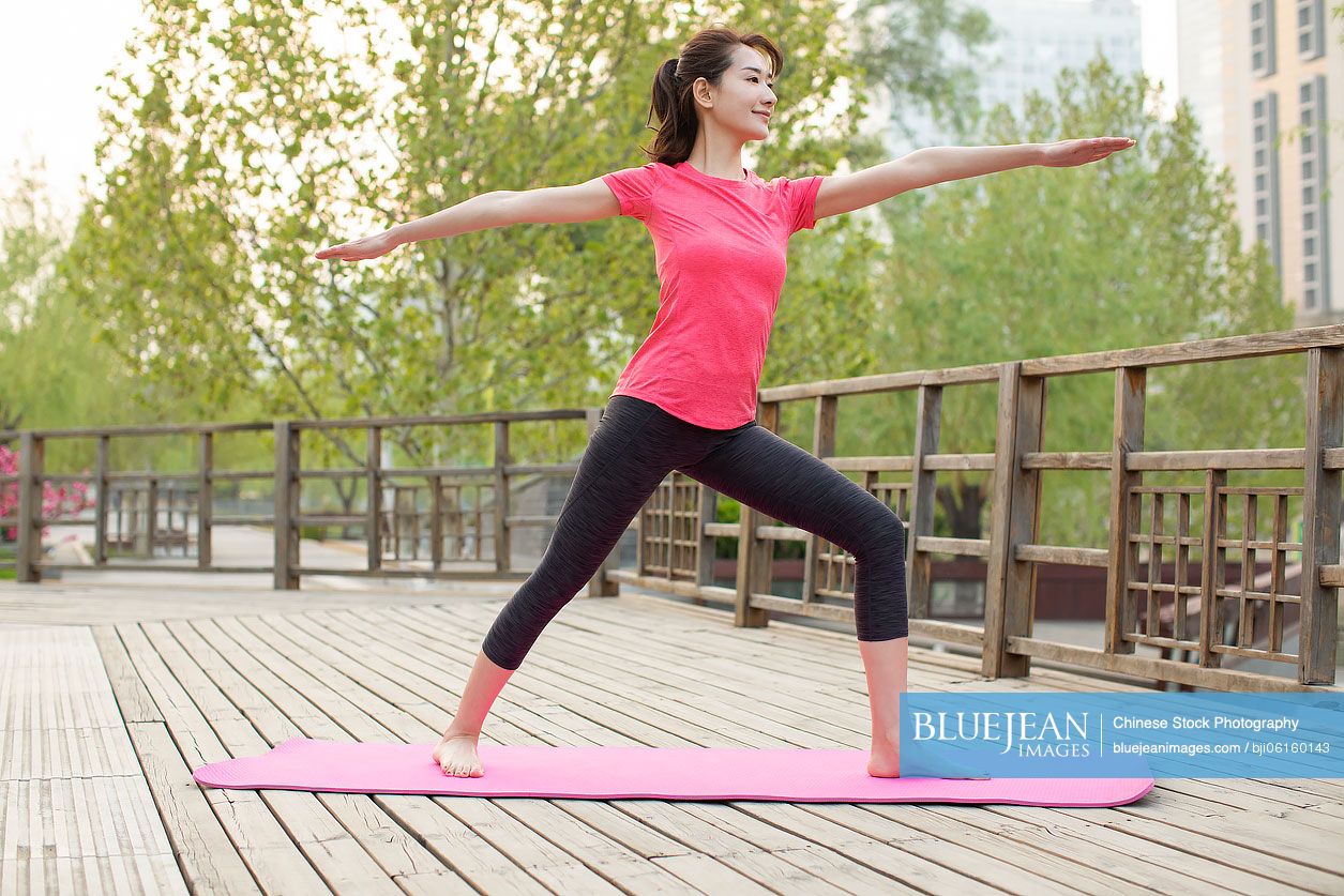 Happy young Chinese woman doing yoga in park