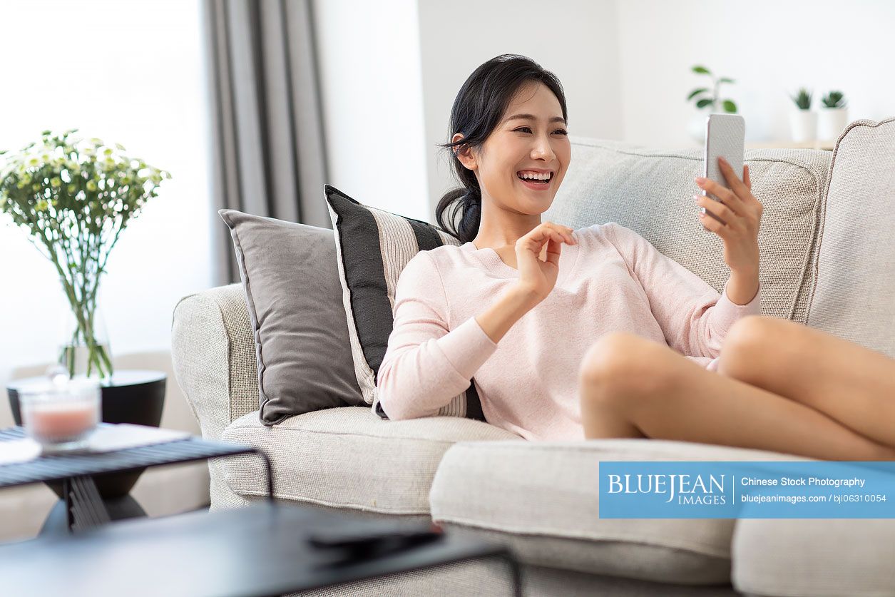 Happy young Chinese woman on video call on sofa