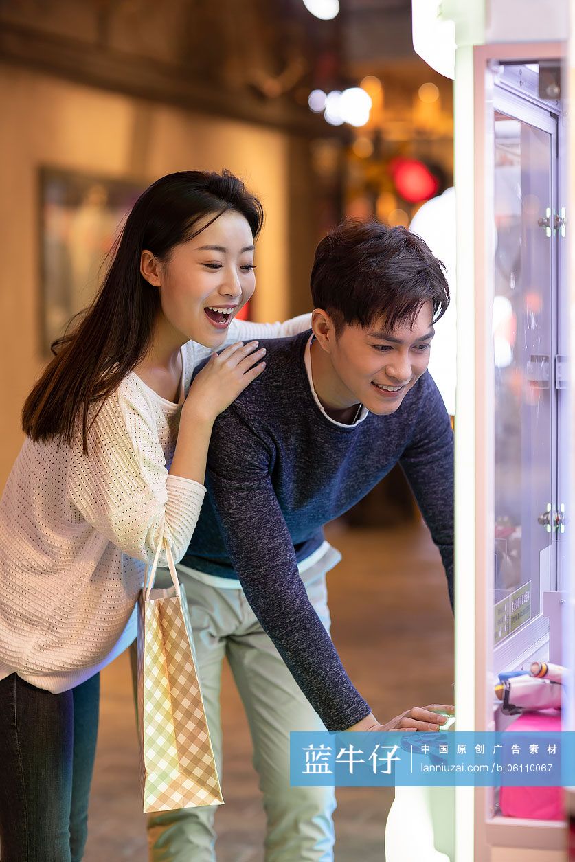 快乐的年轻情侣在商场玩抓娃娃机游戏