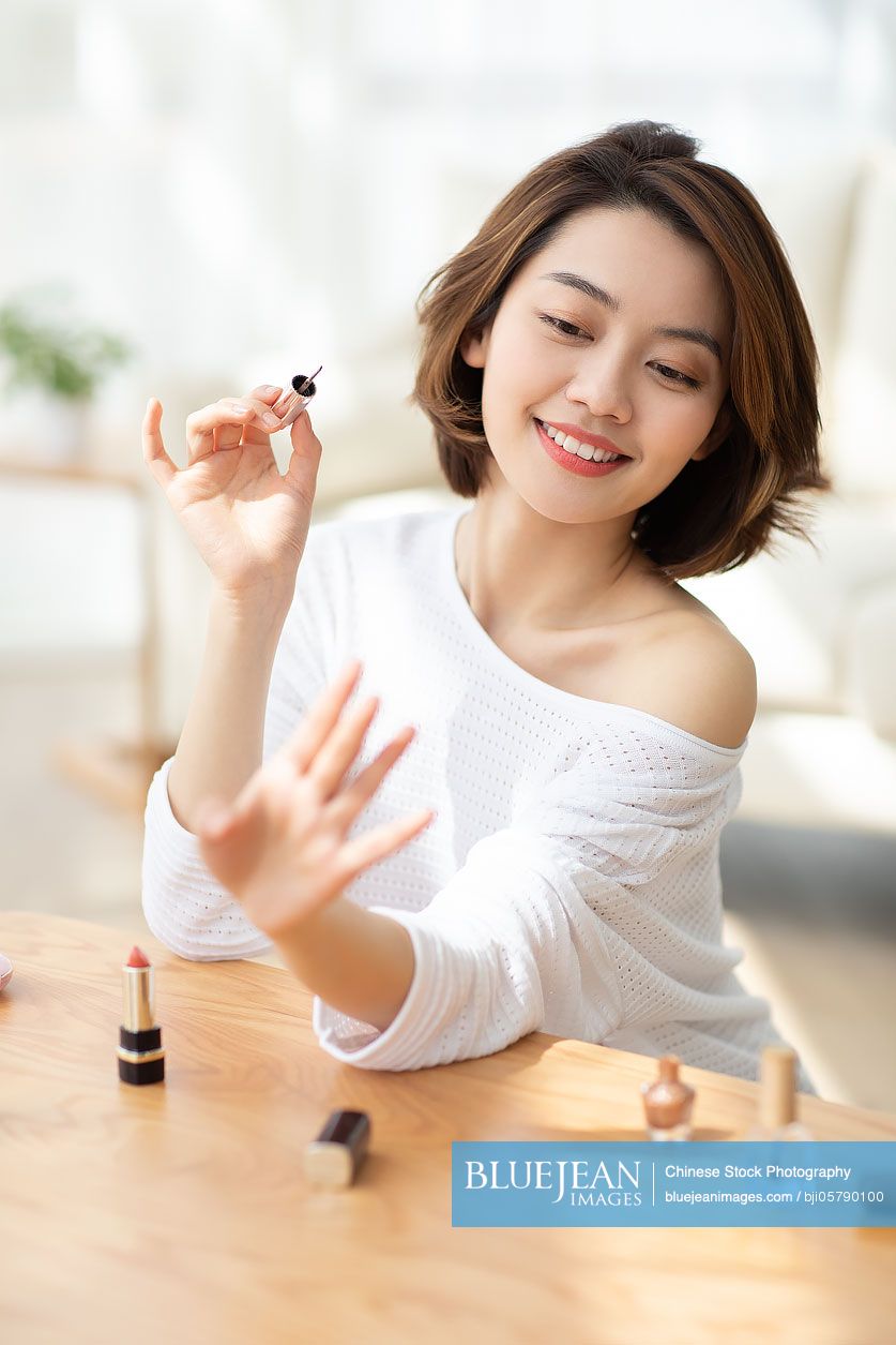 Young Chinese woman applying nail polish at home