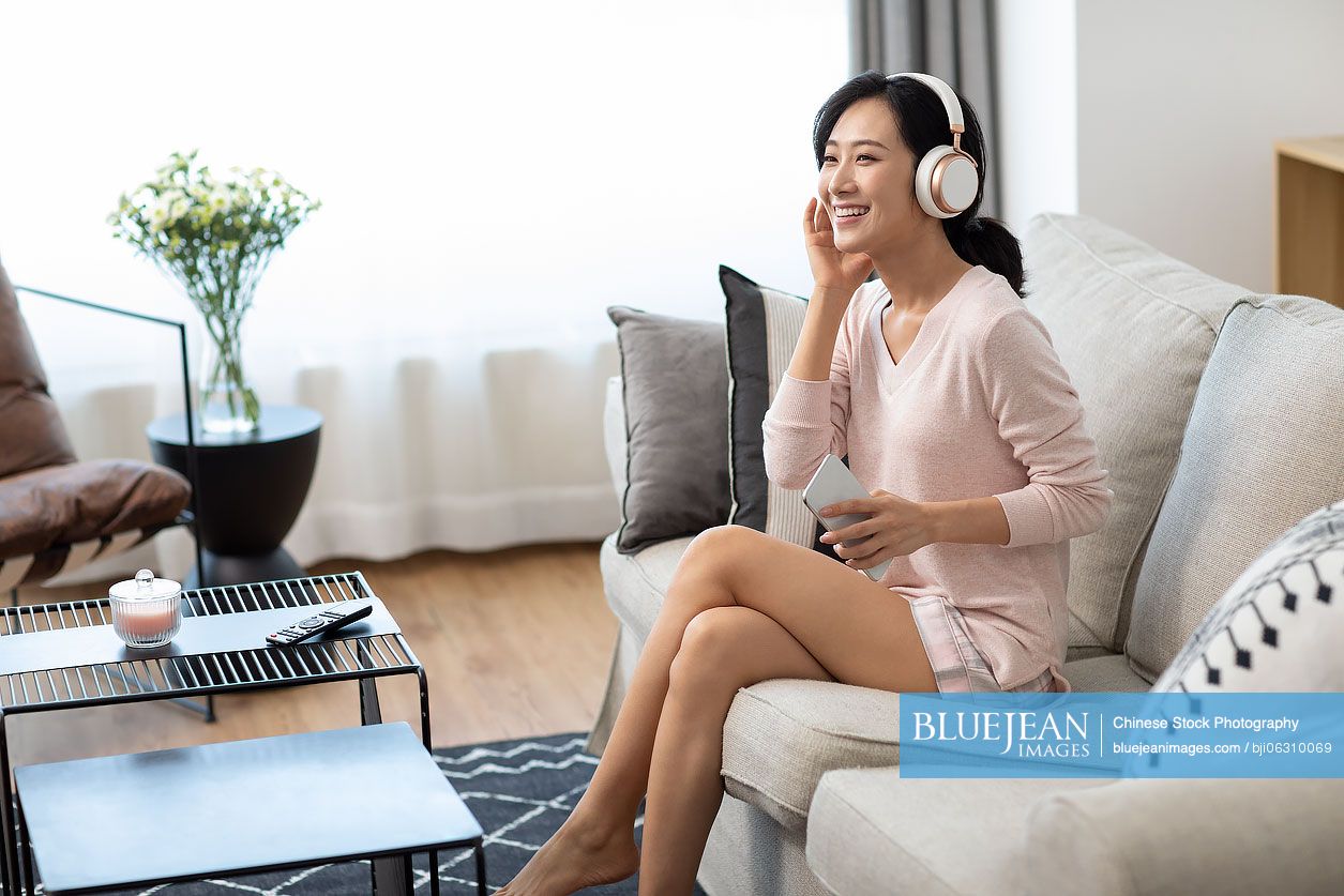 Happy young Chinese woman wearing headphones on sofa