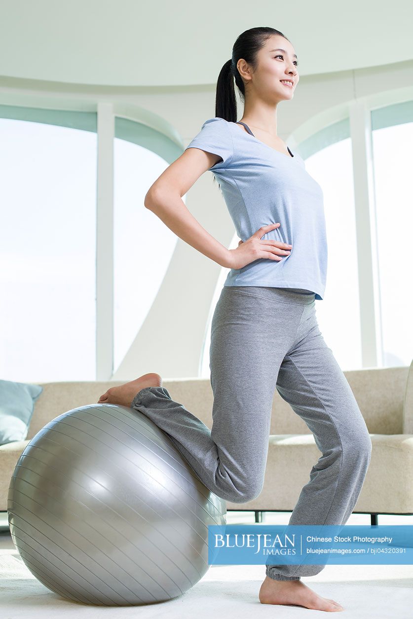 Young Chinese woman practicing yoga with fitness ball