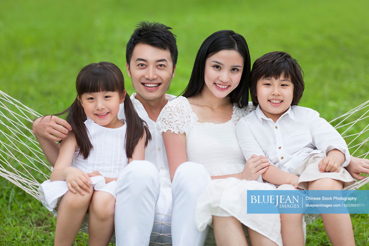 Happy young Chinese family sitting in a hammock outdoors