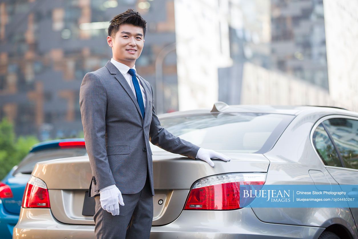Chinese chauffeur standing next to the car
