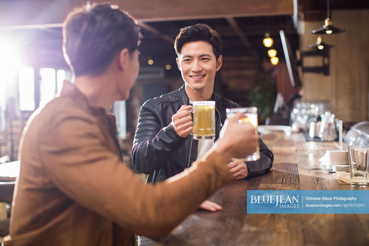 Happy young Chinese men drinking beer in bar