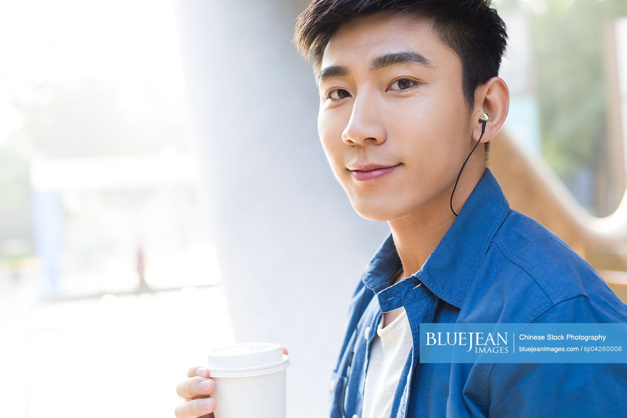 Young Chinese man listening to earphones with coffee