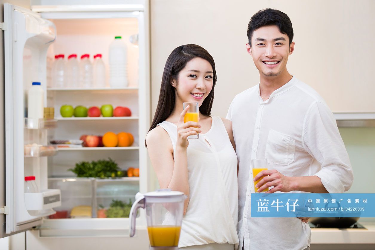 在厨房里端着橙汁的年轻夫妇
