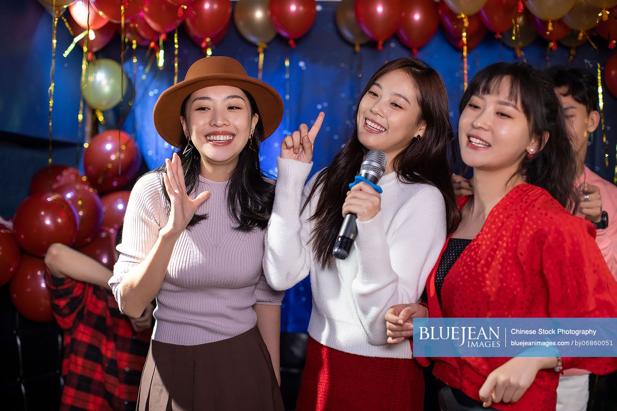 Happy young Chinese friends singing karaoke in nightclub