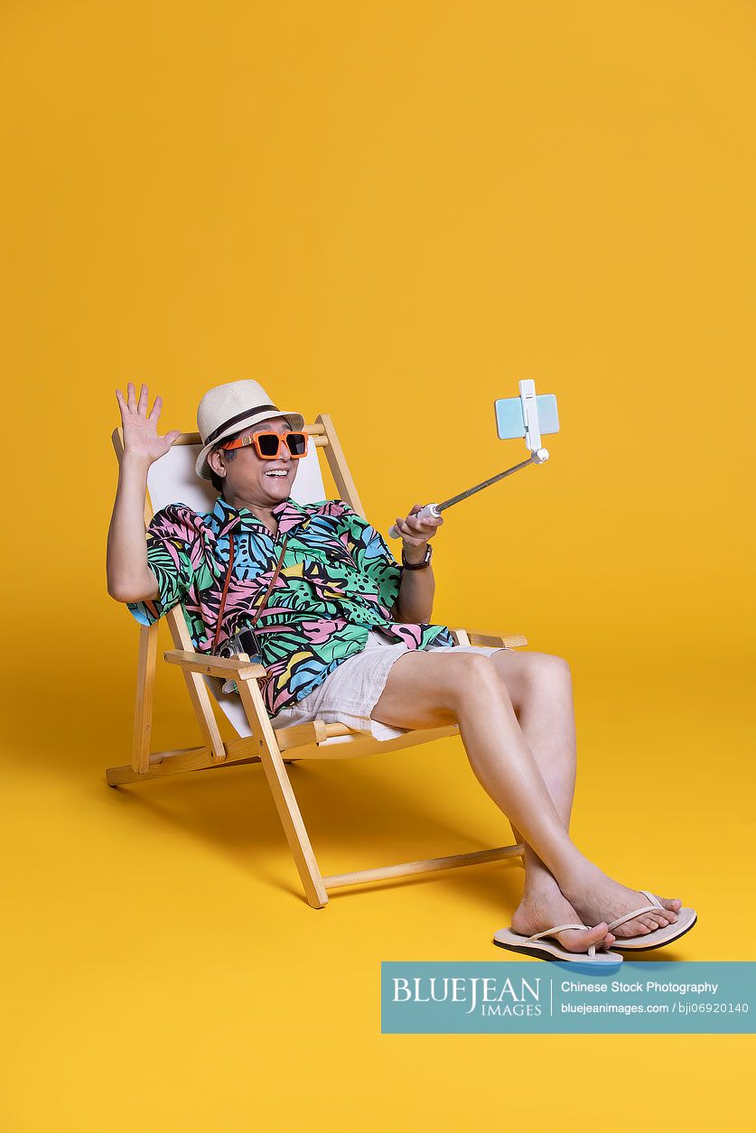 Cheerful senior Chinese man taking selfie with smartphone