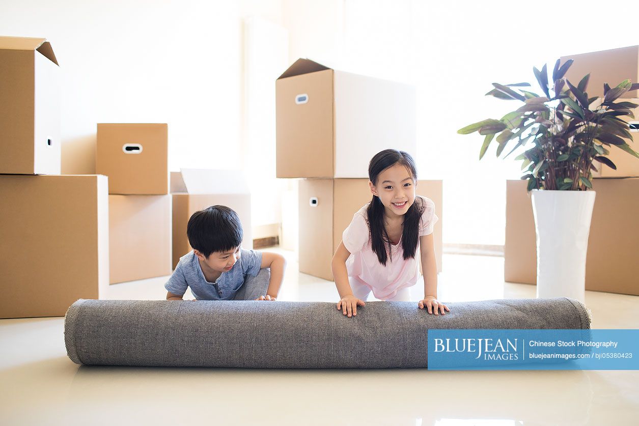 Cute Chinese children unrolling carpet in new house