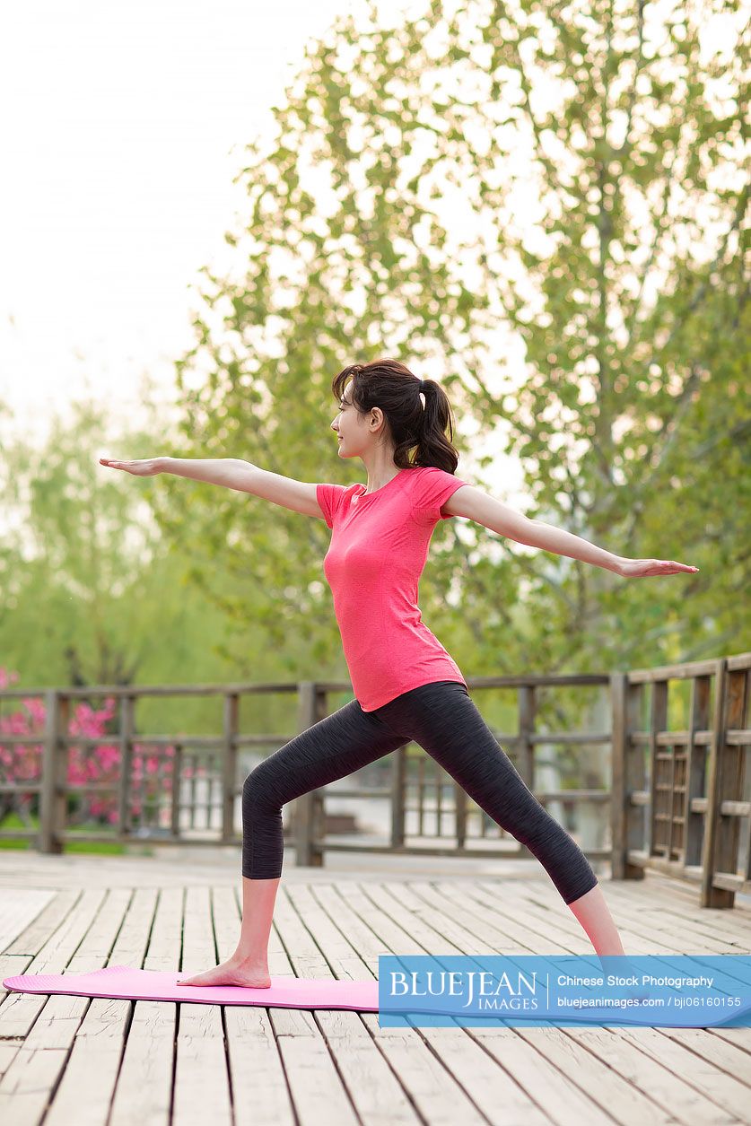 Happy young Chinese woman doing yoga in park