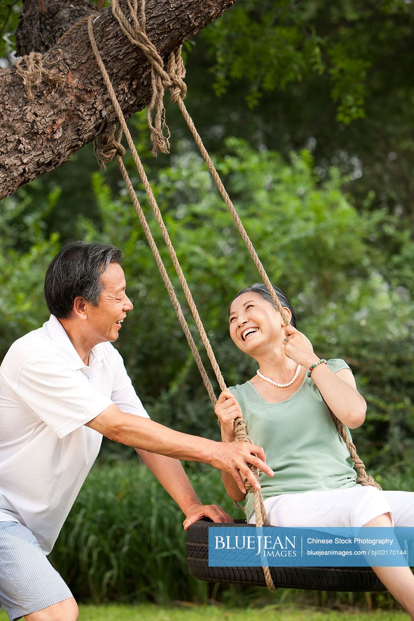 Cheerful senior Chinese couple playing on a swing