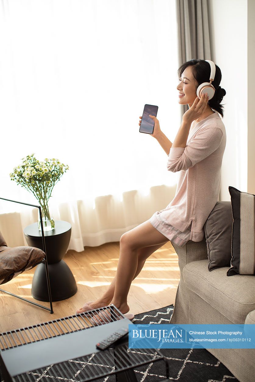 Happy young Chinese woman listening to music in living room