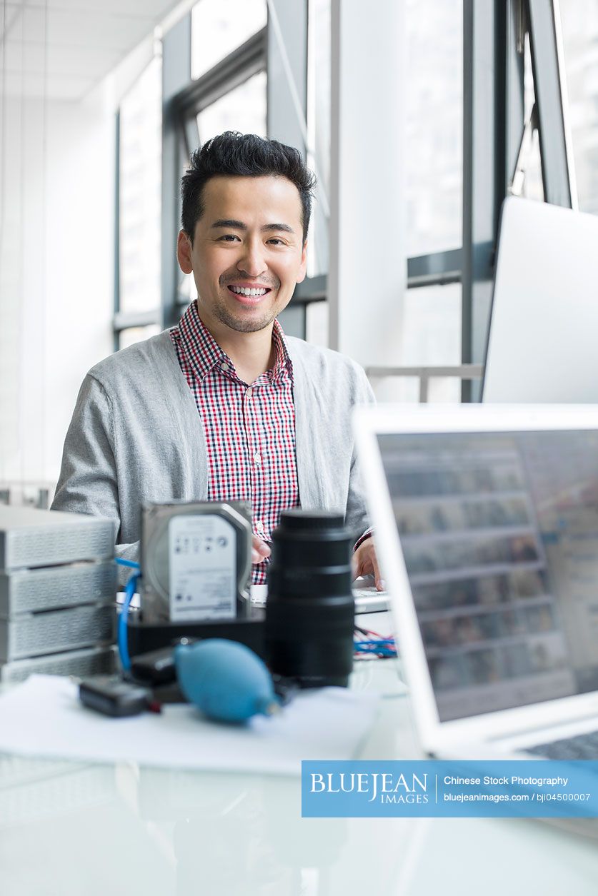 Male Chinese photographer working in office with computer
