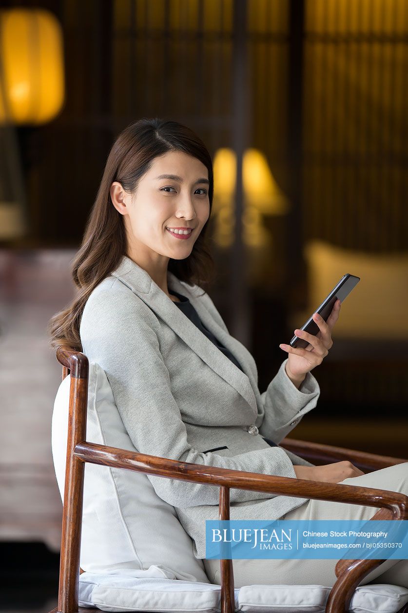 Cheerful young Chinese businesswoman holding a smart phone