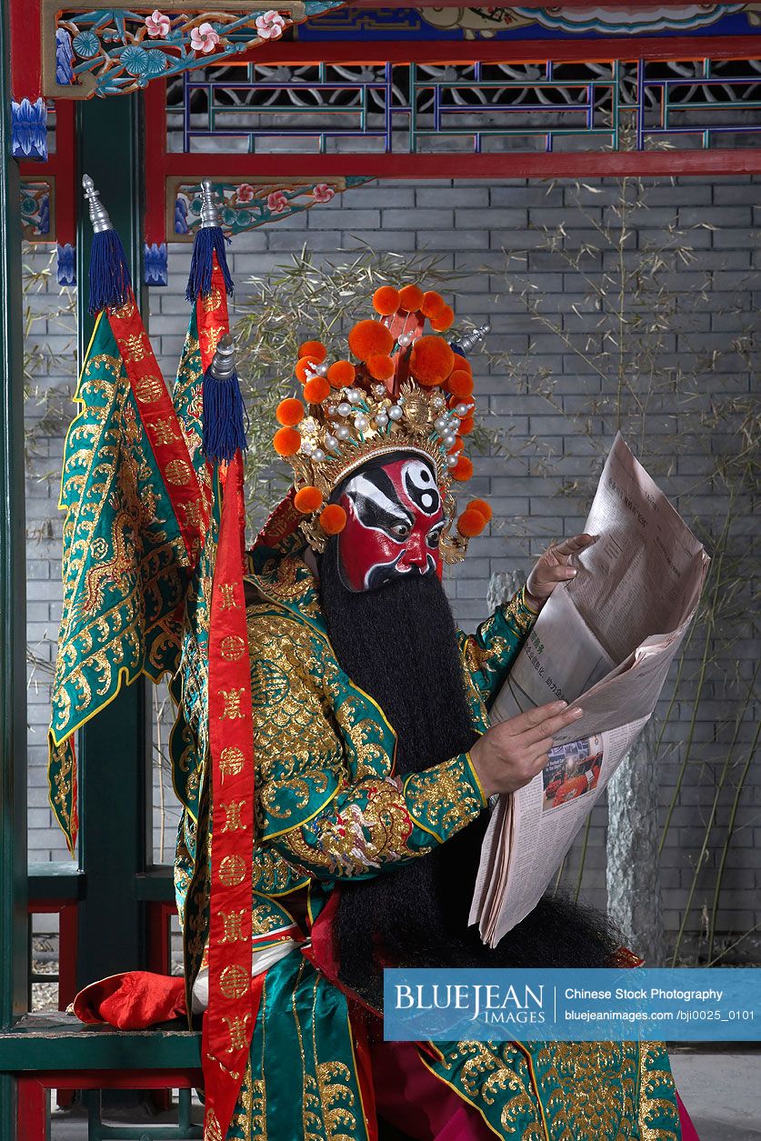 Chinese Man In Ceremonial Costume Reading Newspaper