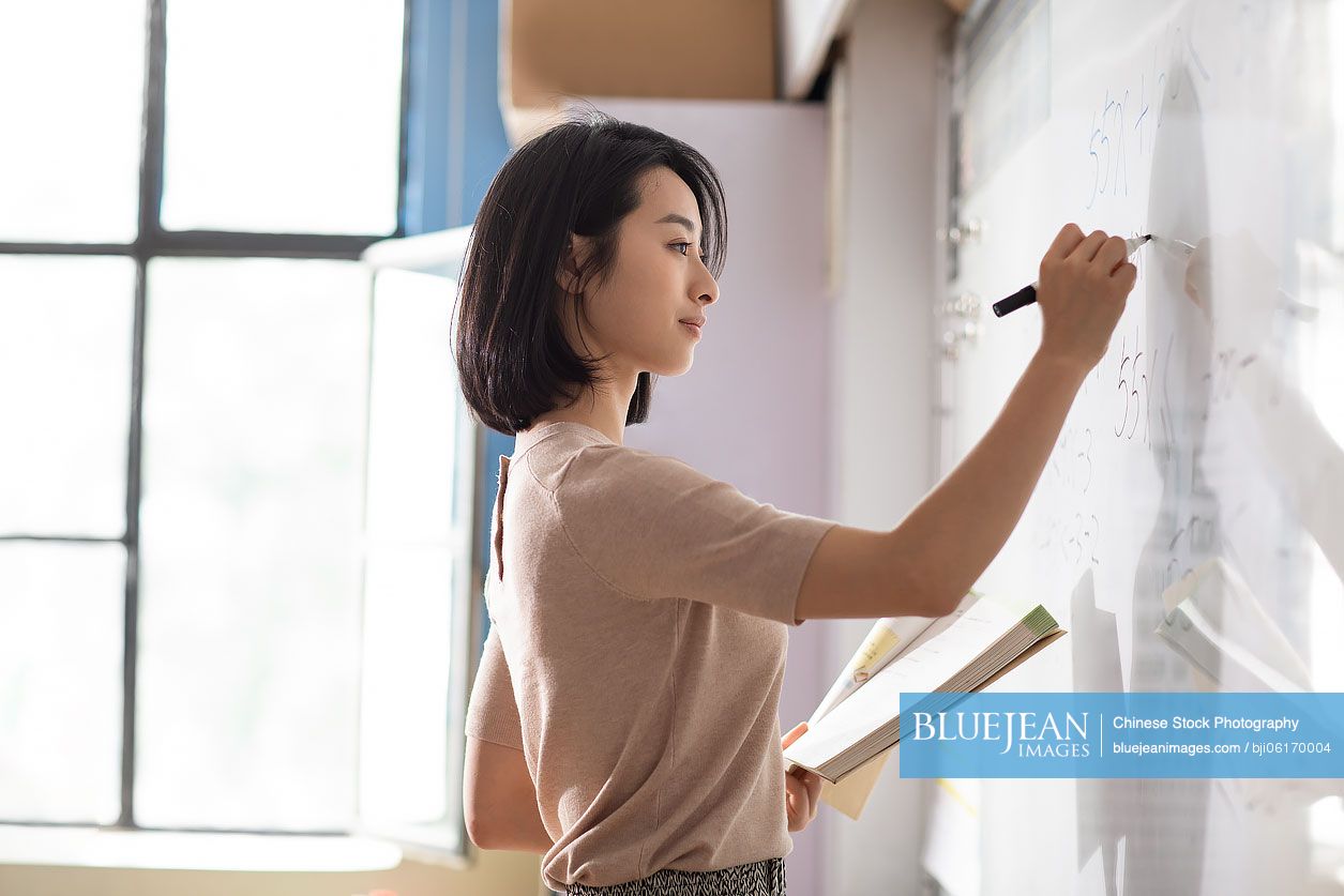 Young Chinese teacher writing on blackboard