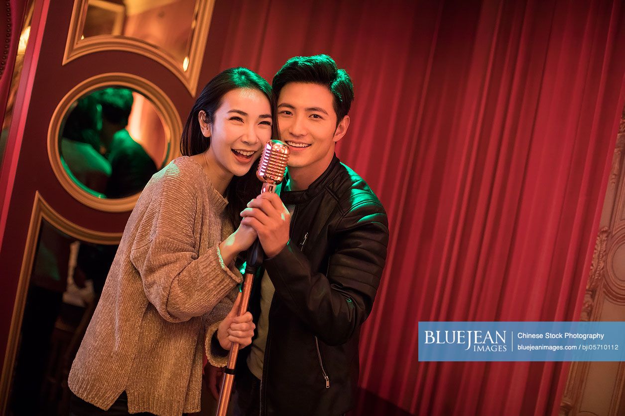 Happy young Chinese couple singing karaoke in nightclub