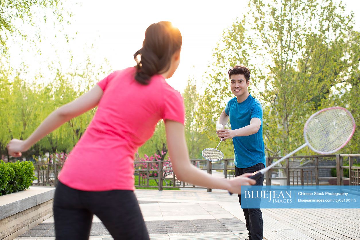 Happy young Chinese couple playing badminton in park