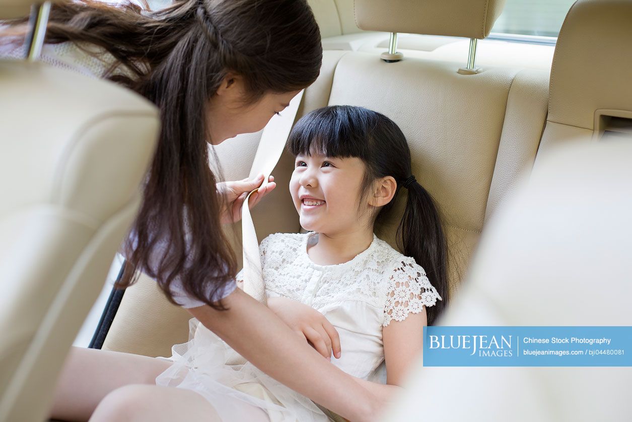Chinese mother fastening seat belt for daughter