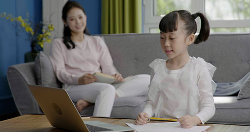 Little girl taking an online class with her mom keeping her company