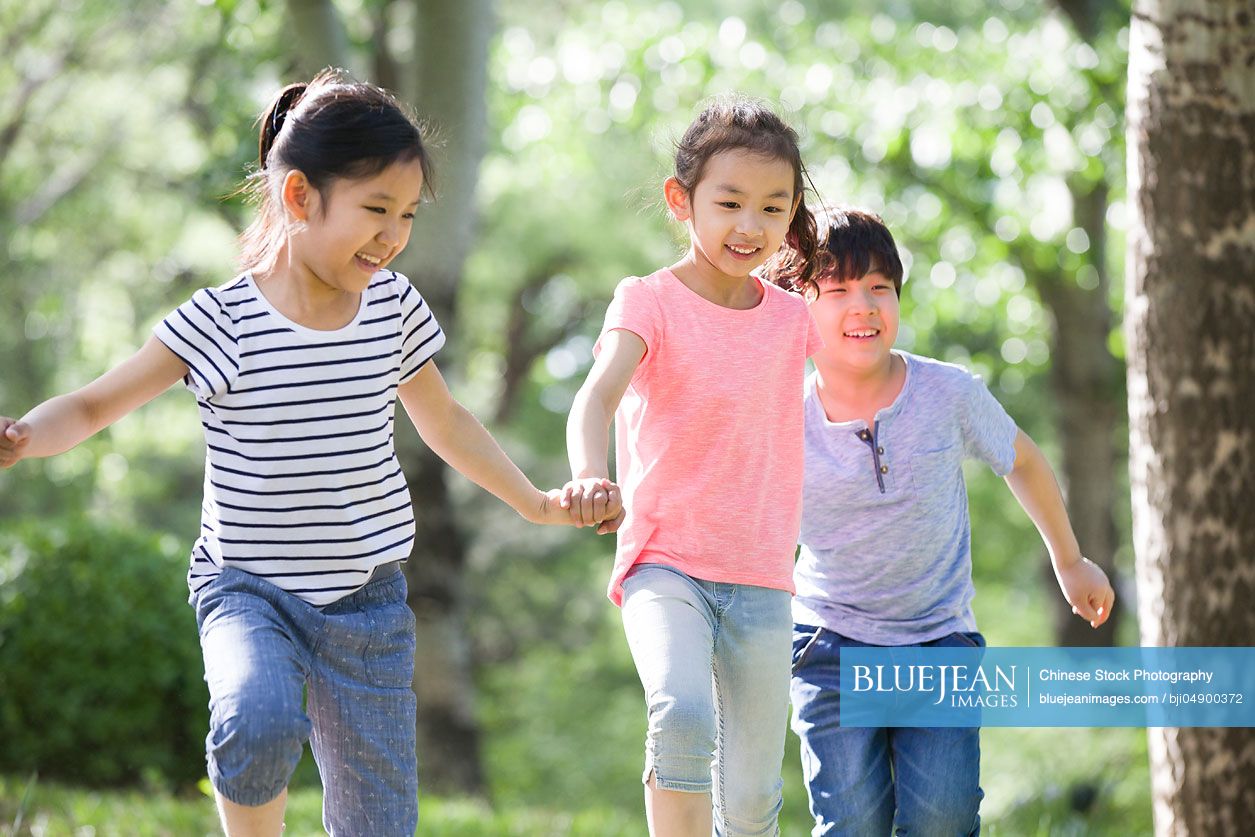 Happy Chinese children holding hands running in woods