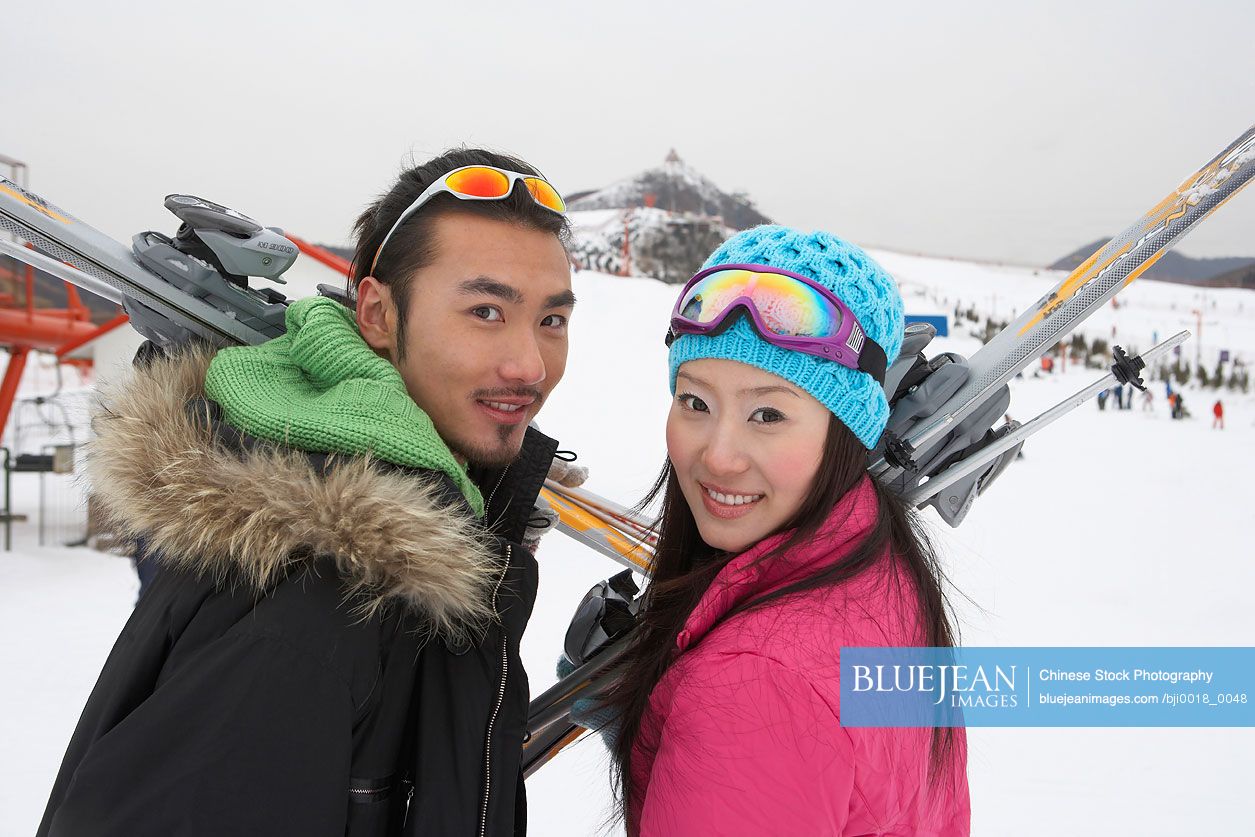 Chinese couple on ski field, holding skis